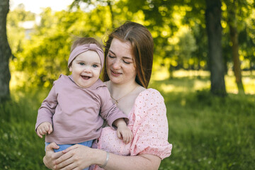 A young mother walks with a one-year-old baby, holds him in her arms, hugs. Communication with the...