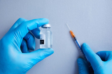 A gloved hands holds a vial of clear vaccine liquid for science with syringe in background