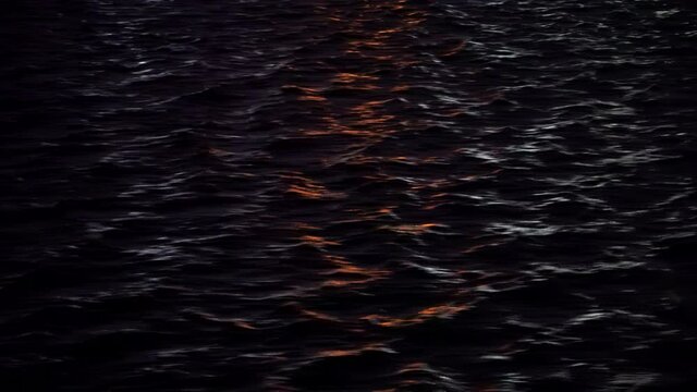 wavy ocean surface in the rays of the setting sun. dark sea water with reflection of red rays of the sun. water background