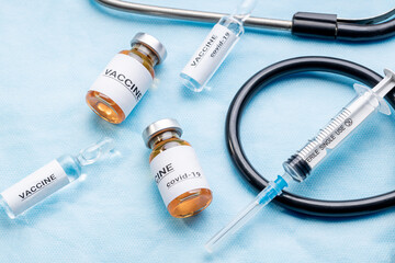 vaccine injecting concept. vaccination bottle with syringe near stethoscope over blue surgery background. above view. illustrative