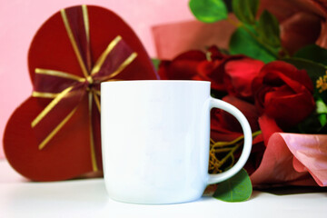 Happy Valentine's Day white coffee tea mug cup, styled with red roses bouquet and heart shape gift against a pink textured background. Mockup. Copy space.