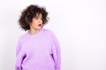 young beautiful caucasian woman wearing pink knitted sweater against white wall stares aside with wondered expression has speechless expression. Embarrassed model looks in surprise