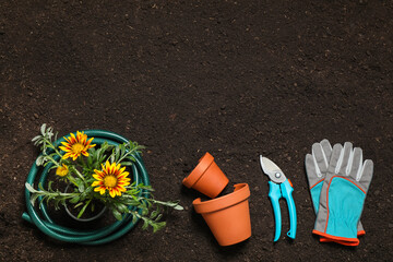 Flat lay composition with gardening equipment and flower on soil, space for text