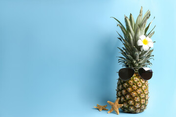 Pineapple with sunglasses, plumeria flower and starfishes on light blue background, space for text. Creative concept