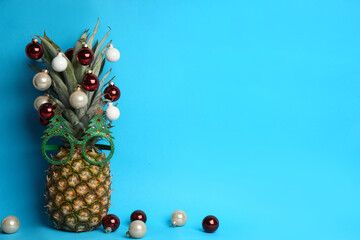 Pineapple with party glasses and Christmas tree balls on light blue background, space for text. Creative concept