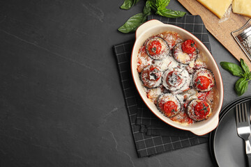 Baked eggplant with tomatoes and cheese served on black table, flat lay. Space for text