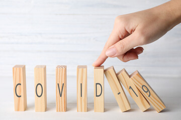 Woman stopping domino effect at white table, closeup. Prevent spreading of coronavirus