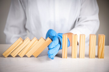 Doctor stopping domino effect at white wooden table, closeup. Prevent spreading of coronavirus