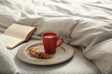 Cup of aromatic coffee, cookies and book on bed with soft blanket