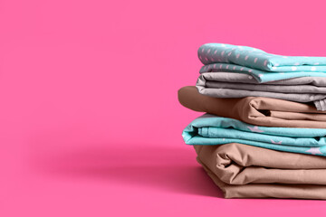 Stack of clean bed sheets on pink background. Space for text