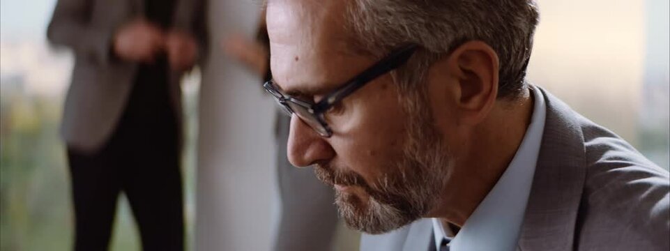 Close-up of mature adult Caucasian businessman face while thinking about solution. Man sitting in office.
