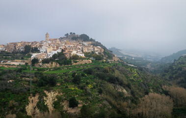 Fototapeta na wymiar Foggy morning at the hill of Polop de Marina with church and castell over green forest, Spain