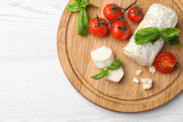 Delicious goat cheese with basil and tomatoes on white wooden table, top view