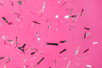 Shiny silver confetti falling down on pink background