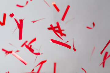 Shiny red confetti falling down on light grey background