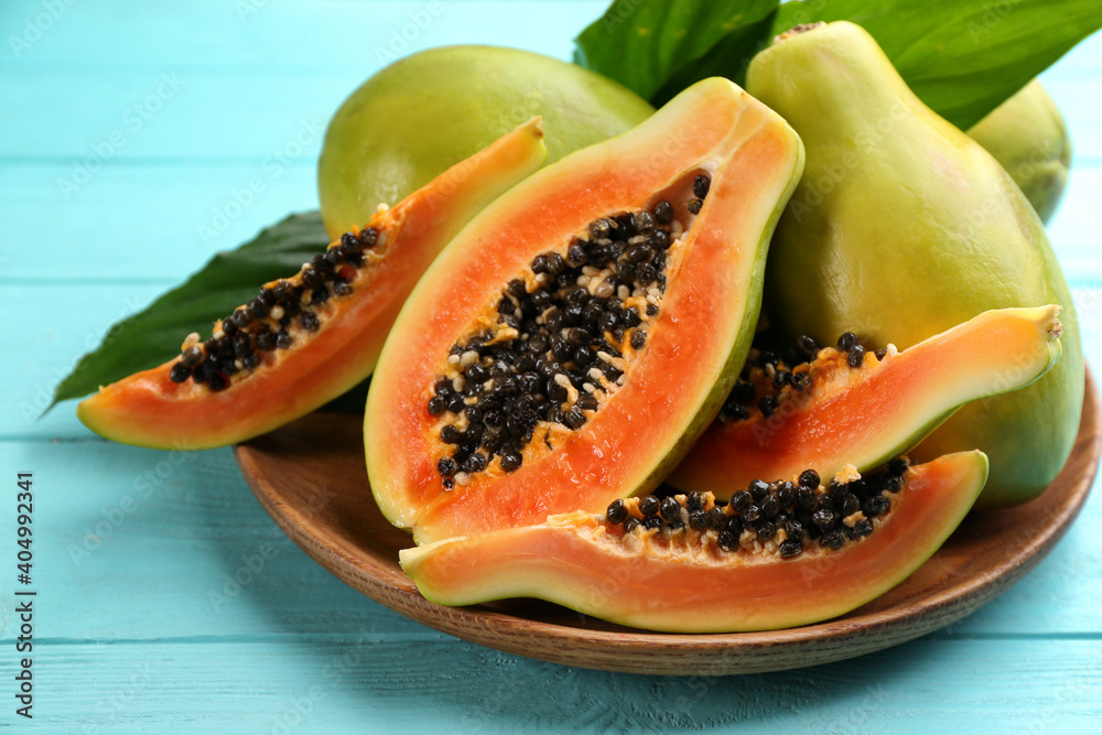 Wall mural fresh ripe papaya fruits with green leaves on turquoise wooden table, closeup