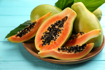 Fresh ripe papaya fruits with green leaves on turquoise wooden table, closeup - obrazy, fototapety, plakaty