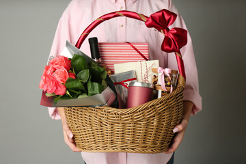 Woman holding wicker basket full of presents on grey background, closeup