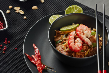 Pad Thai. Thai food. Stir-fried rice noodles with chicken meat, shrimps, peanuts, vegetables and sauce. Setting table.