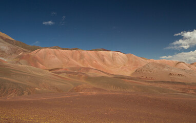 Fototapeta na wymiar Desert landscape high in the Andes mountain range. View of the brown land, dunes and colorful mountains under a deep blue sky. 