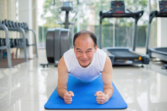 Senior asian man practicing yoga pose on yoga mat and background blur diverse equipment and machines at the gym room. Fitness, sport, Advertising concept