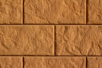 Full frame texture background of a modern golden brown stone block wall with large blocks and a sunlit textured surface
