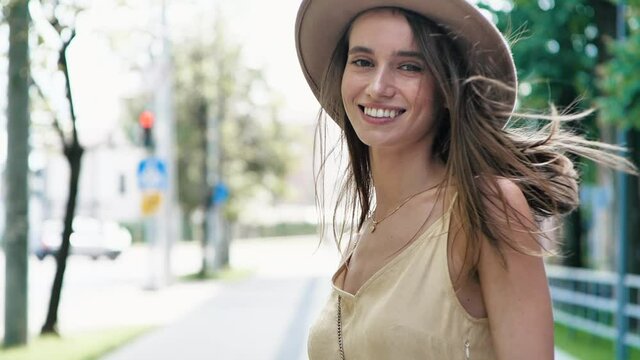 Young Attractive Female model turning to the Camera, Happy and Satisfied. Sun Rays touching Girl hair while she jumps full of Happiness and Pleasant. Gorgeous Woman in trendy Hat. People. Emotions.