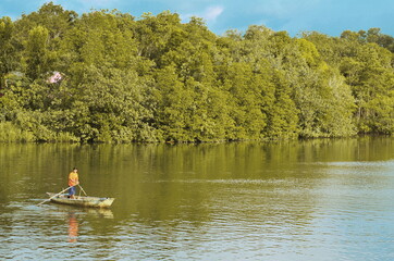 Fototapeta na wymiar Mid Adult Man Standing In Boat On Lake Against Trees