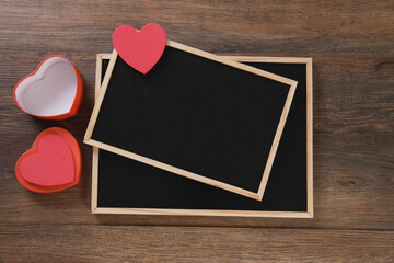 Red heart-shaped gift box and blackboard on wooden background with space