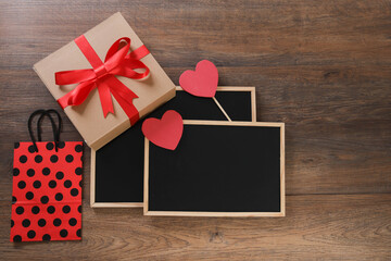 blackboard with shopping bag, gift and hearts on wooden background with space