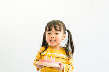Cute adorable little asian toddler girl celebrating birthday while holding birthday cake wooden toy gift and blowing candles.Happy birthday party.isolated on white background at home.Happy Birthday.