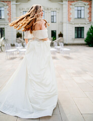 cheerful beautiful woman in white wedding dress whirls near beautiful building.