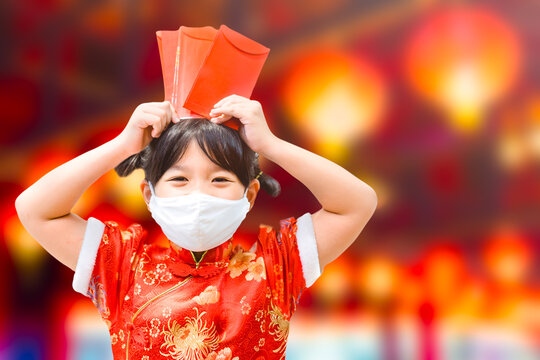 Happy chinese new year girl.Asian young girl wearing mask with traditional cheongsam qipao dress showing red envelope at home.Happy chinese new year during covid19 lockdown.stay safe home in holiday.