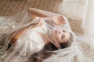 a beautiful young woman in robe is lying under a veil.