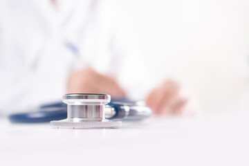 Gray stethoscope on cardiogram. Blurred doctor cardiologist in white uniform writes prescription during medical appointments at clinic. Healthcare and medicine concept. 