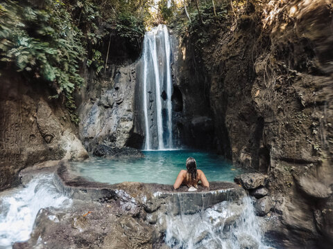 Woman in blue bikini sitting on water near waterfalls