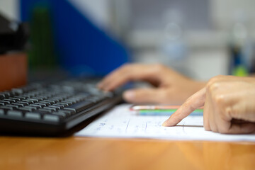 Close-up action of at person's finger in pointing to correct the data on paper with blurred background of the another hand typing on keyword to input data in computer. Business working photo. - obrazy, fototapety, plakaty