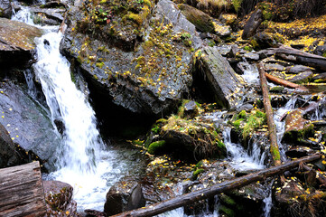 A stormy mountain stream flowing downward bending around stone boulders.