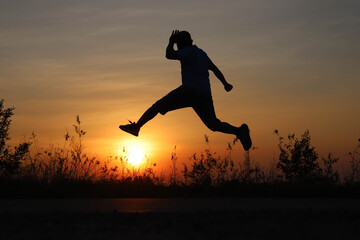 The cheerful young man jumped high and stepped on the sun in the silhouette.
