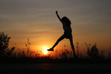 The cheerful little girl jumped high above the sun in a silhouette.