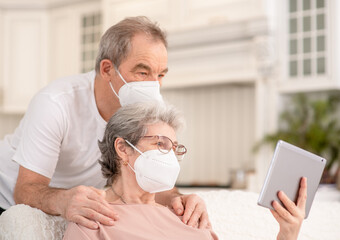 Senior couple wearing protective masks having video chat on tablet computer during the coronavirus epidemic
