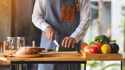 Closeup image of a female chef cutting and chopping vegetables by knife on wooden board in kitchen