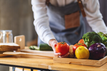 A female chef holding and picking a fresh tomato from a vegetables tray on the table
