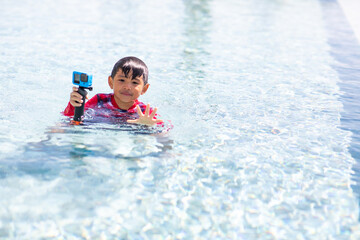 Fototapeta na wymiar Happy family holiday time. Funny Asian little boy splashing swimming in the pool.