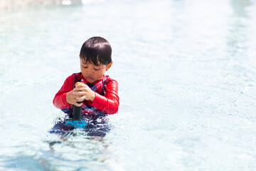 Happy family holiday time. Funny Asian little boy splashing swimming in the pool.