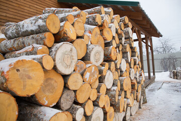 A large pile of round firewood is piled up outside the village house. Snow lies on the wood. Heating concept in the winter season.
