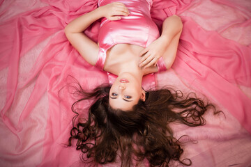 Naklejka premium Portrait of an attractive woman in a pink dress lying on the hem of a dress, top view.