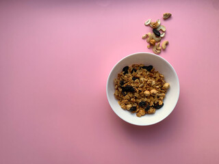 White bowl with homemade granola on a soft pink background. Photo with a top view. Proper nutrition, healthy breakfast.