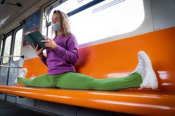 Very flexible woman wearing mask reading book in the subway car sitting in the gymnastic split....