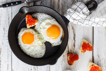 Breakfast with fried eggs in a cast-iron pan with sandwiches with red caviar, top view
